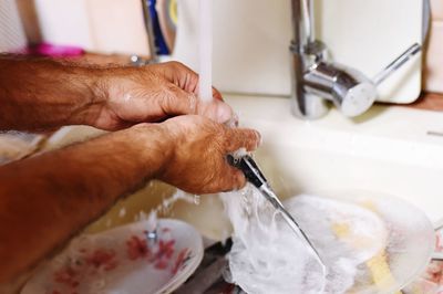 Cropped hands of man washing knife in sink at home