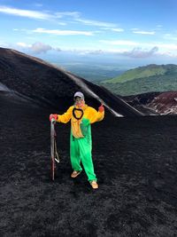 Woman in protective workwear standing with plank on mountain against sky