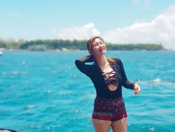 Portrait of smiling woman standing at beach against sky