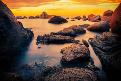 Rocks in sea against sky during sunset