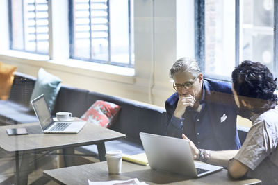 Businessmen discussing over laptop computer seen through window