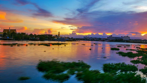 Scenic view of river by buildings against sky during sunset