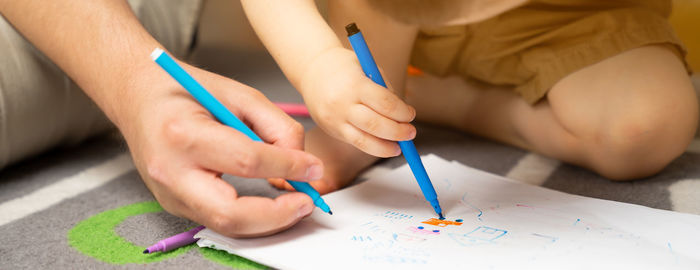 Little toddler boy of two or three years old with dad draws with markers in the album 