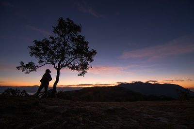 Silhouette woman standing by tree against sky during sunset