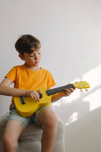 Cute boy learns to play the yellow ukulele guitar in home. cozy home.