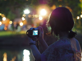 Woman photographing by lake at night