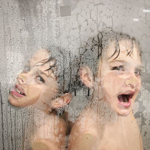 Kids playing in the shower faces against steamed glass