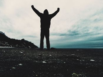 Low angle view of person with arms raised standing on field against sky at dusk