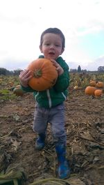 Full length of cute boy holding pumpkin on field against sky