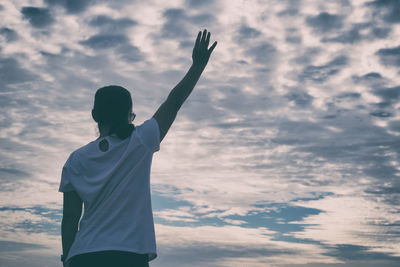 Rear view of woman with arms raised standing against cloudy sky