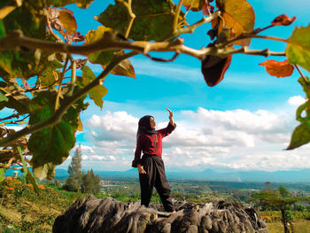 Woman shielding eyes while standing against landscape