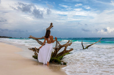 Rear view of woman standing on beach against sky