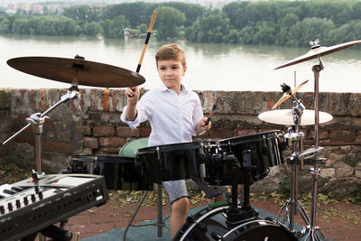 Boy playing drum kit against river