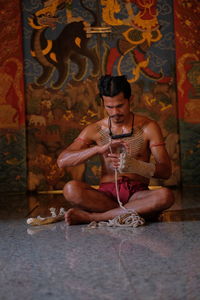 Shirtless man wrapped rope on hand in temple