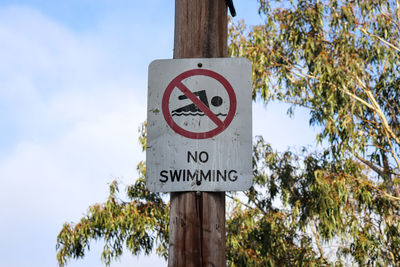 Low angle view of no swimming sign against sky