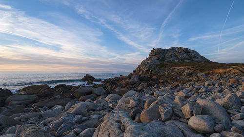 Rocks on beach against sky during sunset