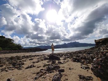 Man standing on rock at beach against sky