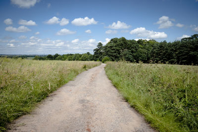 Dirt road amidst field against sky