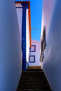 Low angle view of staircase amidst buildings against blue sky