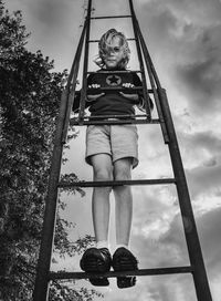 Low angle view of child standing on ladder against sky