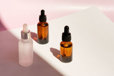 Three transparent amber and frozen glass dropper bottles with liquid inside on pink background 