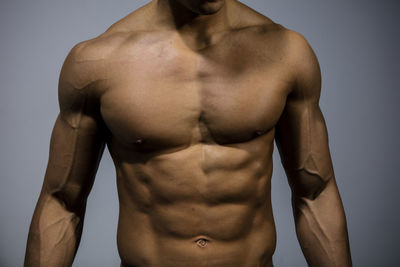 Midsection of shirtless muscular man standing against wall