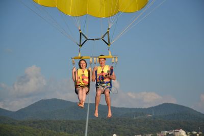 Full length portrait of smiling couple parasailing against sky