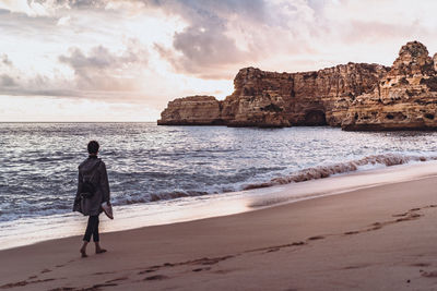 Rear view of woman walking on beach against sky