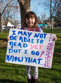 Full length portrait of girl holding text in paper while standing on field