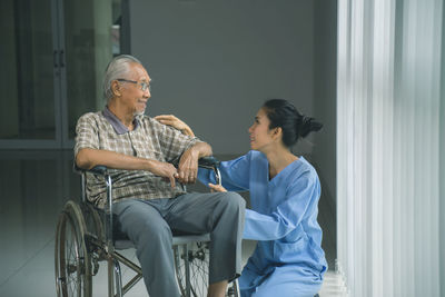 Nurse talking with senior man sitting on wheelchair in hospital