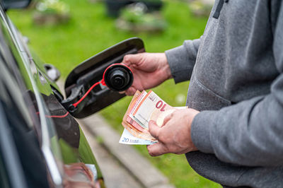 A man s hand counts money while standing at an open fuel tank, the concept of rising fuel prices