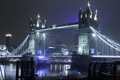 Illuminated bridge over river in city at night