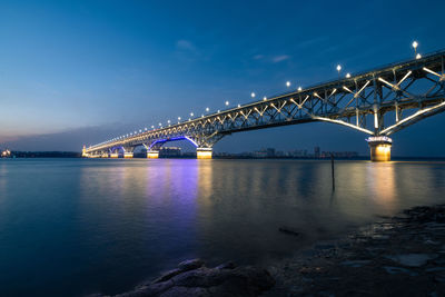 Illuminated bridge over river against sky at dusk