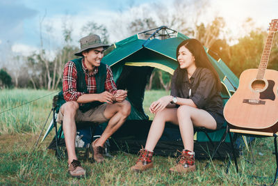 Young woman sitting with male friend by guitar against camping tent