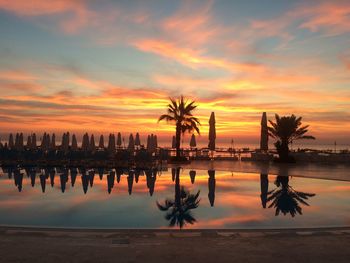 Silhouette palm trees by swimming pool against sky during sunset