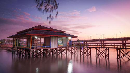 Houses on pier by sea against sky during sunset