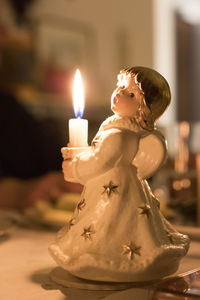 Close-up of illuminated candle with figurine on table