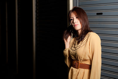 Young woman standing against shutter at night