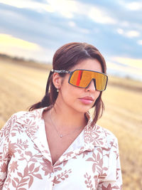 Young woman wearing sunglasses standing on field against sky 