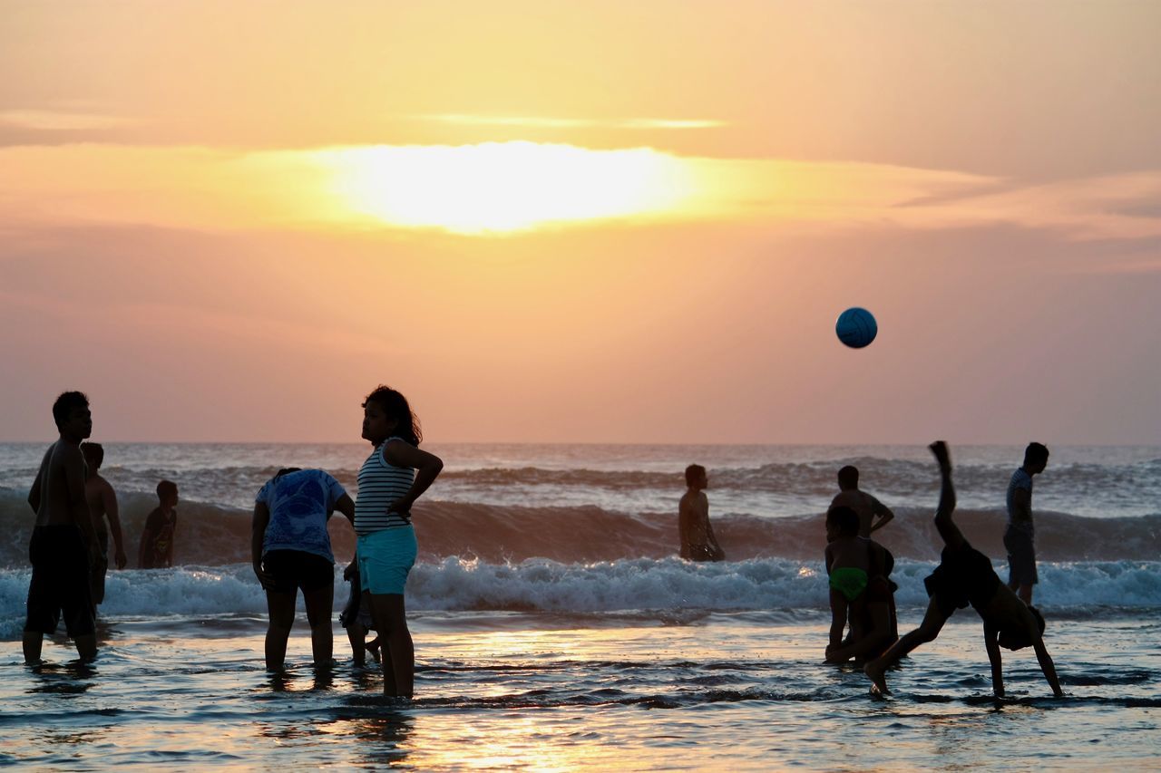 sunset, sea, sky, water, group of people, beach, beauty in nature, land, horizon over water, scenics - nature, lifestyles, real people, leisure activity, men, sport, orange color, playing, horizon, nature, sun, outdoors