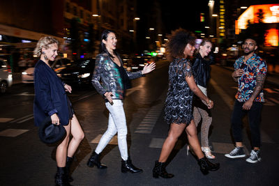 Group of stylish multiracial friends walking together on city street for party at night