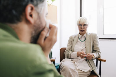 Female psychotherapist discussing with male patient sitting at therapy office