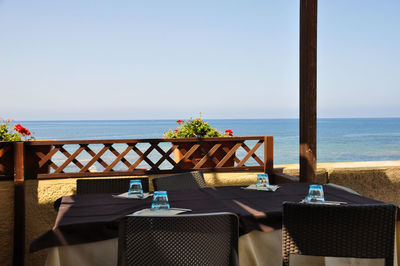 Chairs and table at beach against clear sky