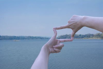 Cropped hands of person making frame against sky