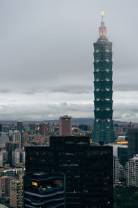 Illuminated buildings in city against cloudy sky