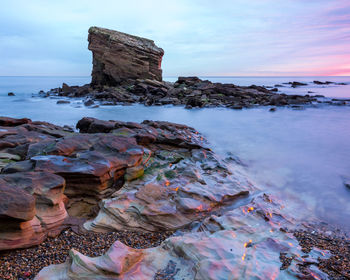 Rocks on beach against sky during sunset