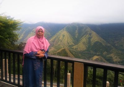 Portrait of woman standing on railing against mountains