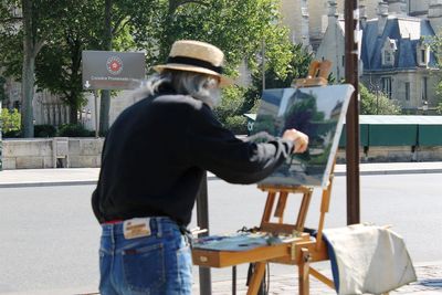 Rear view of man holding hat standing against wall