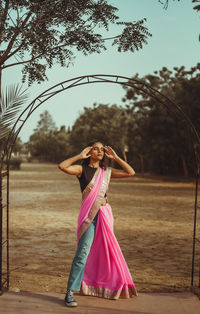 Woman standing by pink umbrella against trees