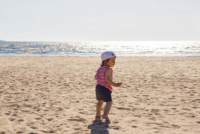 Child in a t-shirt and shorts walks on the beach near the sea